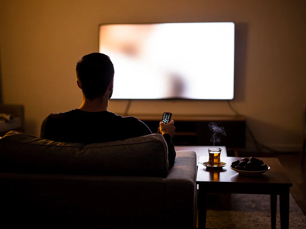 Un homme consulte le guide TV de son IPTV depuis son salon, un thé à la menthe posé sur la table basse